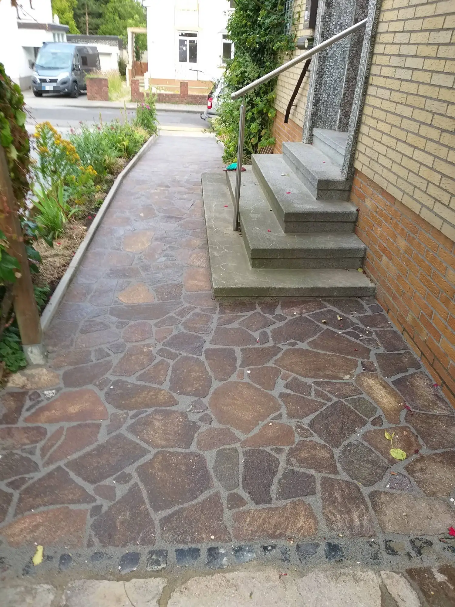 Neu verlegter Weg aus Natursteinpolygonplatten neben einer Eingangstreppe